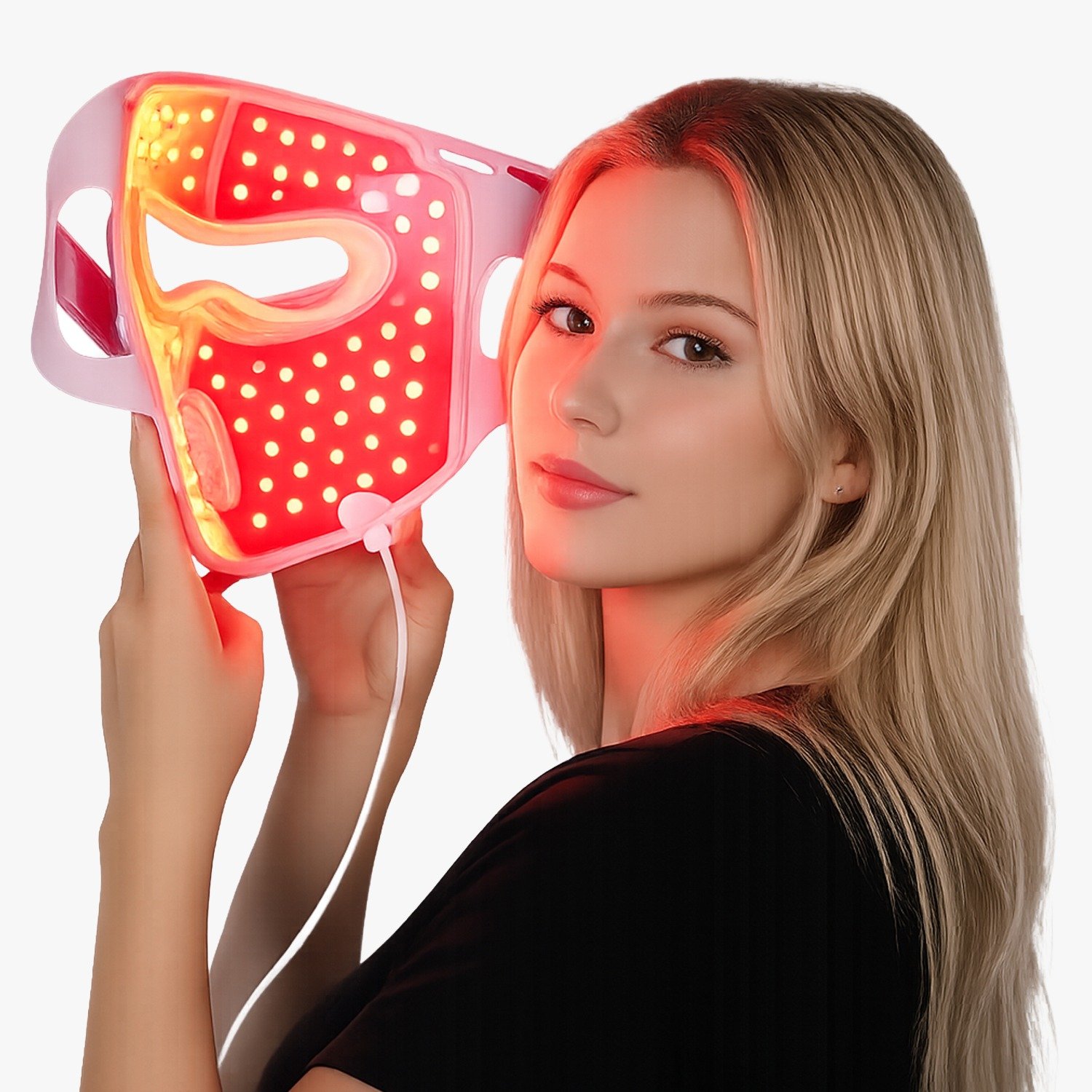 Young woman holds a red LED face mask near her cheek, smiling slightly. The mask glows red with numerous lights for facial therapy.